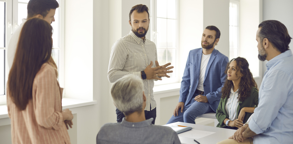 En mand taler til en gruppe, der ser interesserede på ham. Nogle sidder, andre står op.