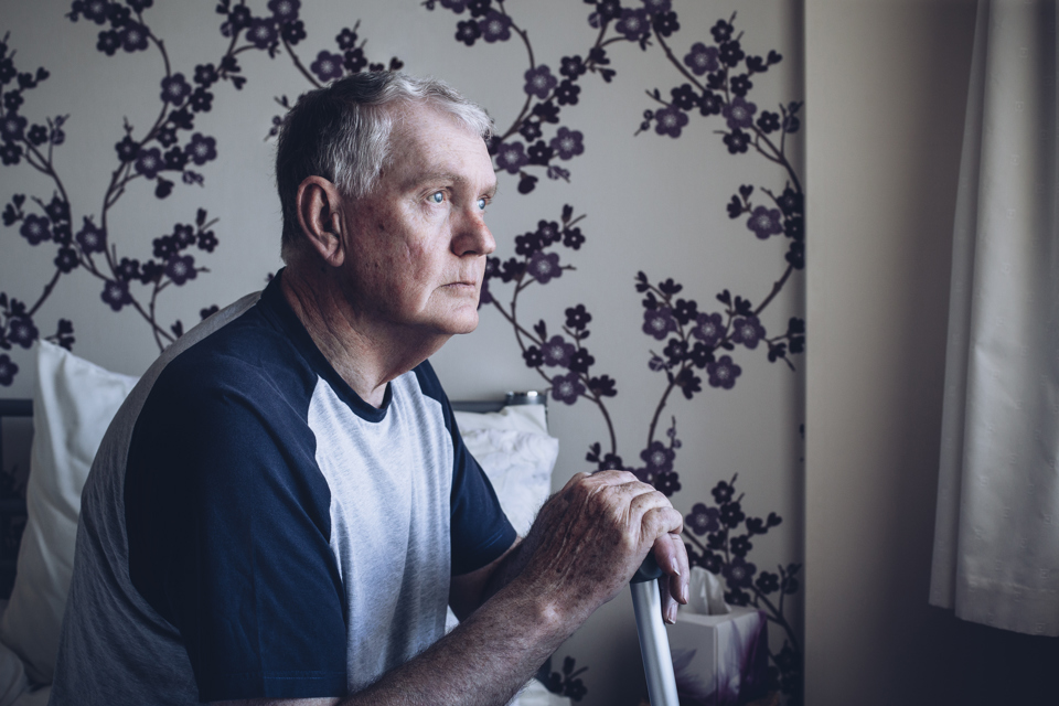 ældre mand ser ud af vindue - han ser trist ud