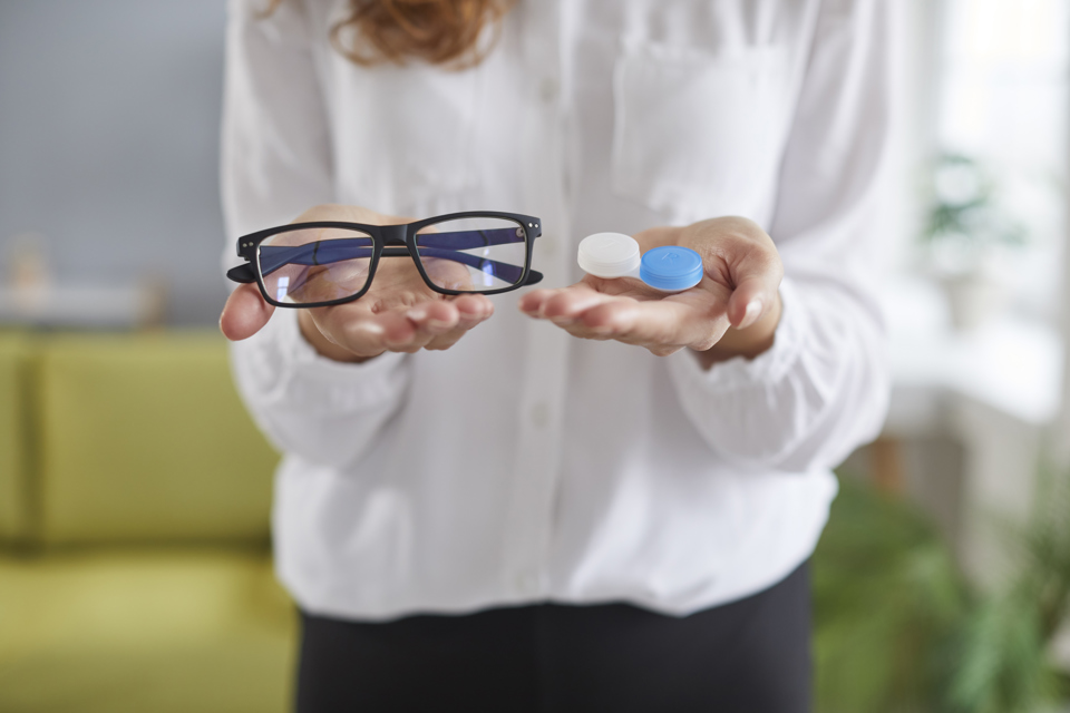 en person holder et par briller og et sæt kontaktlinser