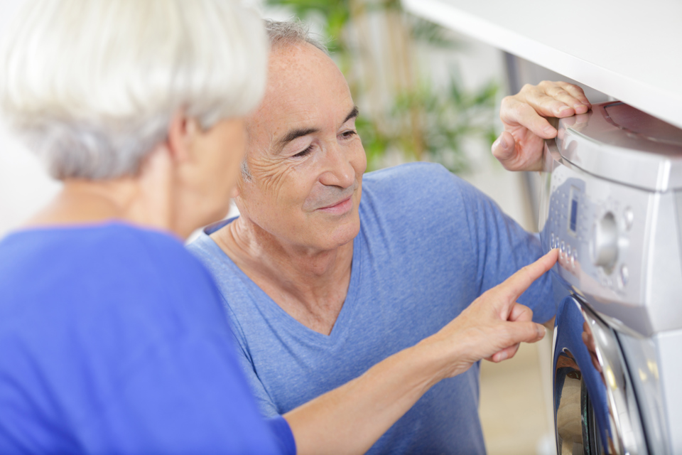 kvinde instruerer ældre mand i brug af vaskemaskine