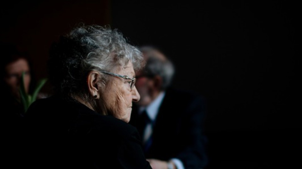 Kvinde sidder i mørke, man kan se, der sidder nogen et stykke fra hende, men hun ser ikke på dem